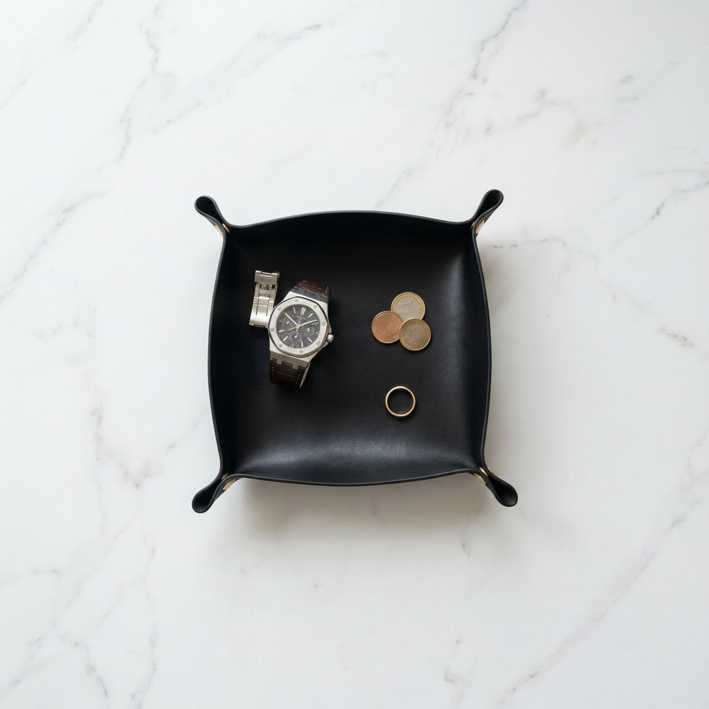 Doctor Desk black PU leather foldable valet tray holding a watch, coins, and a ring on a white marble surface